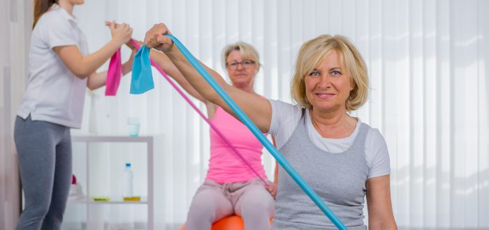senioren machen übungen mit dem theraband auf dem pezziball